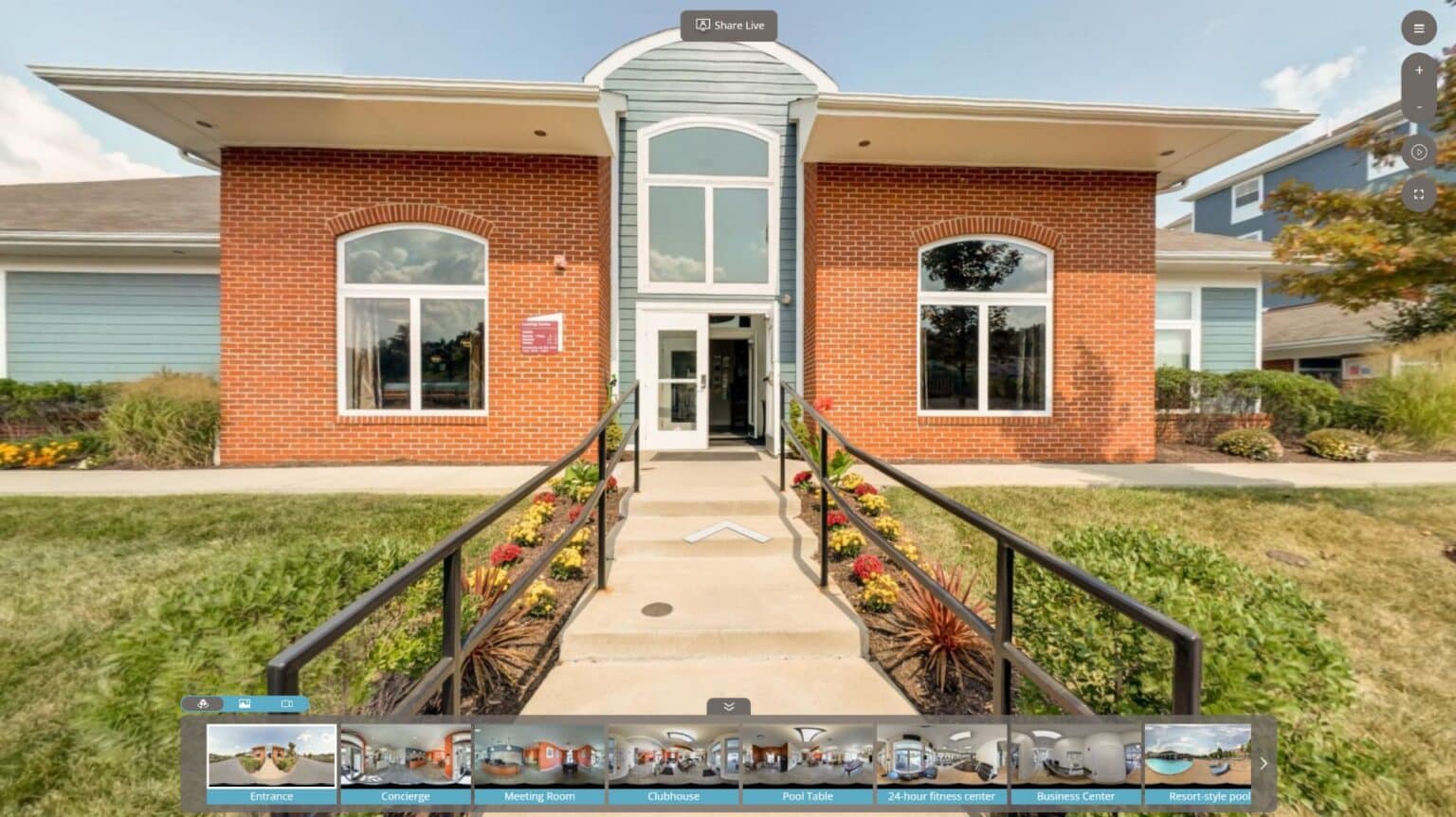 Exterior view of a brick building with large windows, a central glass door, and a ramp leading to the entrance, surrounded by manicured landscaping.